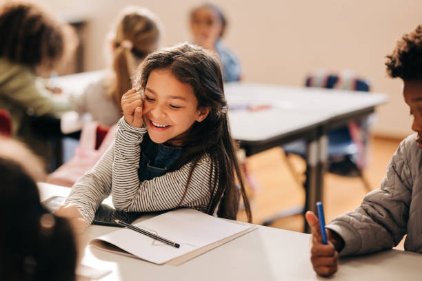 Small girl laughs happily in a primary school class Small girl laughs happily in a primary school class, she is sitting at a table with her her classmates. Elementary school students enjoying an art and creativity class in a child development centre. kids laughing stock pictures, royalty-free photos & images
