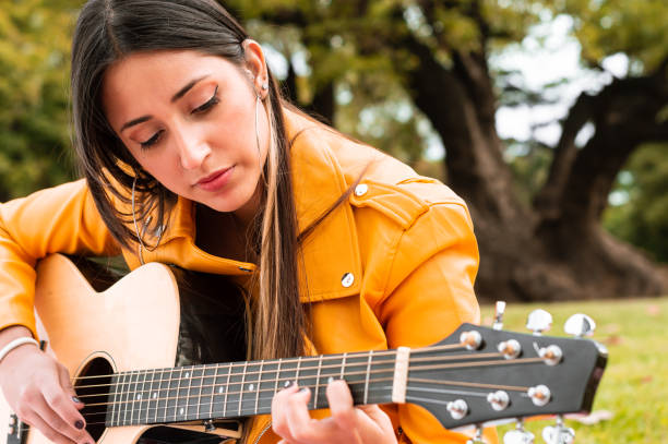 side view of young latin woman playing guitar looking at the strings and her hand making the chord stock photo
