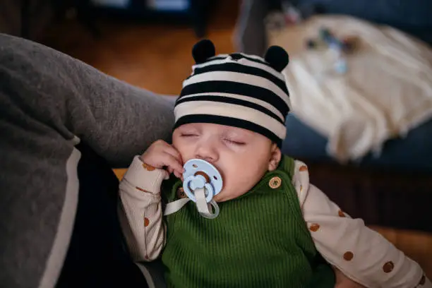 Photo of A Cute Baby Boy With Pacifier Sleeping In His Unrecognizable Parent's Arms