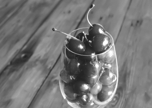 Cherries in a glass. Black and white foto. On a wooden background is a glass with berries. Summer berries are a healthy food. fresh cherry juice.