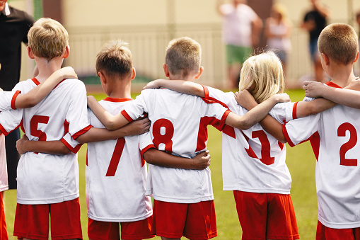 Children's soccer football team. Athletic boys teammates in junior soccer team united in team standing together at grass sport field. Kids in white soccer jersey shirts