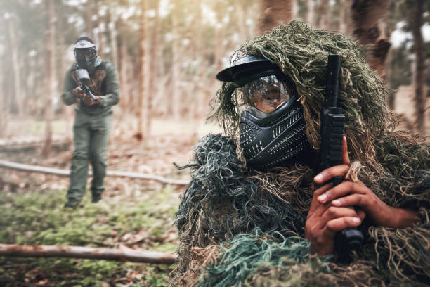 military, camouflage and people on a field playing paintball for exercise, fun and sport in mexico. fitness, action and person hiding while on battlefield for a game, competition or war with friends - paintballing violence exercising sport imagens e fotografias de stock