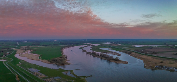 Panoramic aerial view on the river IJssel and Reevediep Bypass waterway during a springtime sunset in Overijssel. The flow of the river is leading towards the setting sun in the distance while lights are popping up in the city at the end of a beautiful springtime day.