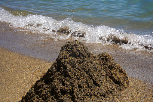 A pile of wet sand on the seashore. The surf gradually erodes the sand castle.