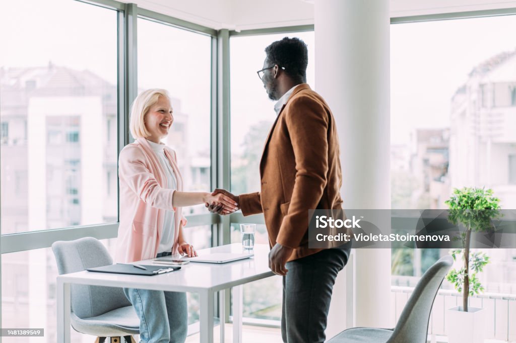 Successful partnership. Business people shaking hands in the office. Photo of one cheerful businessman and one happy businesswoman handshaking across the table. Recruitment Stock Photo