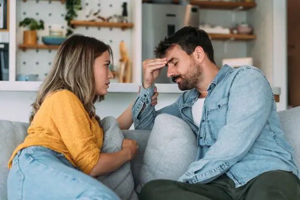Photo of Worried couple talking together in the living room at home.
