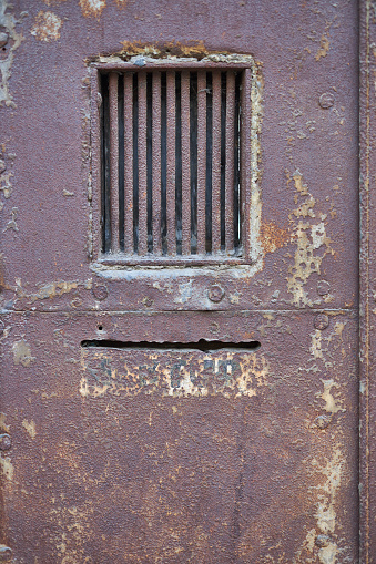 A rusty red old metal steel door in a back alley concrete block abandoned warehouse building.