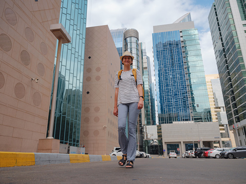 travel to the United Arab Emirates, Happy young asian female traveler with backpack and hat in downtown street of Abu Dhabi. Vacation and tourist destination concept.