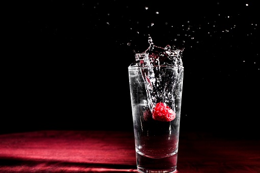 A close-up image of a single raspberry falling into a glass of water, creating a splash of liquid
