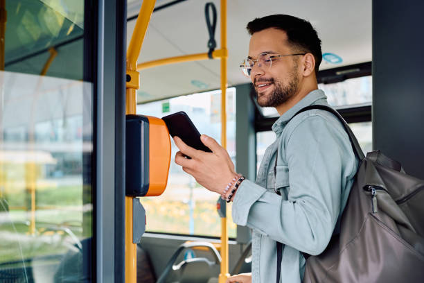 Happy man paying with smart phone while onboarding in public transport.