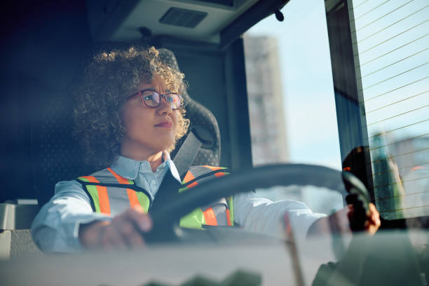 istock Female bus driver driving in reverse while looking in side view mirror. 1481400827