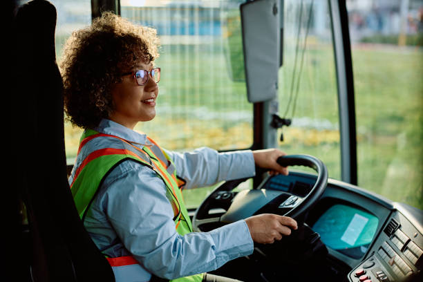 mulher feliz dirigindo um ônibus em marcha à ré enquanto olha para o espelho retrovisor. - motorista de ônibus - fotografias e filmes do acervo