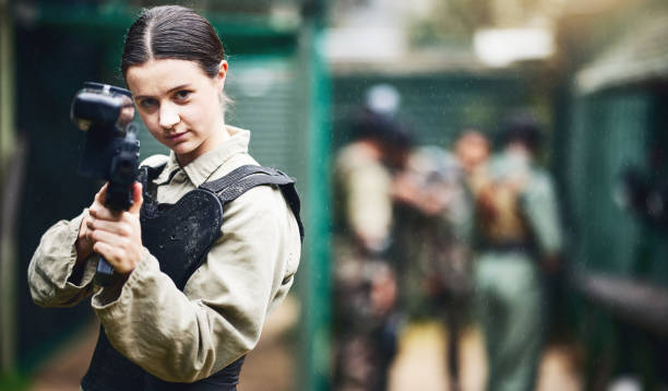 ritratto di paintball, donna e pistola puntano nell'arena di gioco, leadership o lavoro di squadra sportivo in uniforme militare. giocatore, tiratore e fucile da gioco per l'addestramento di guerra di soldati, persone o eserciti nella sfida dei giochi - paintballing violence exercising sport foto e immagini stock