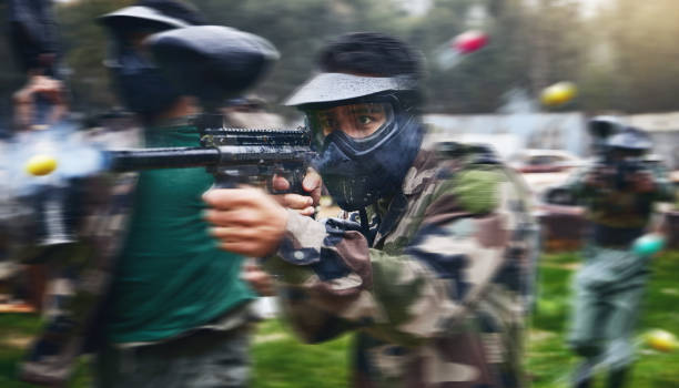 paintball gun, shooting and men in camouflage with safety gear at military game for target practice. teamwork, sports training and war games, play with rifle and friends working together at army park - paintballing violence exercising sport imagens e fotografias de stock