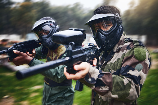 Training, paintball gun and men in camouflage with safety gear at military game for target practice. Teamwork, shooting sports and war games, play with rifle and friends working together at army park