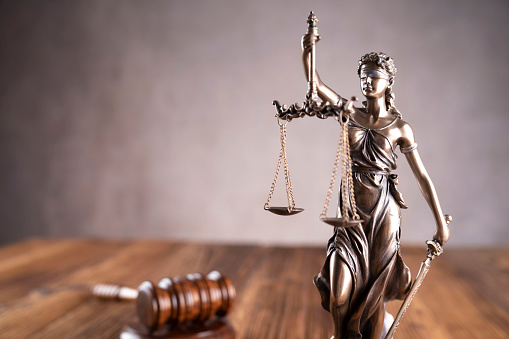 Gavel, scale and Themis sculpture on the rustic wooden desk. Gray background.