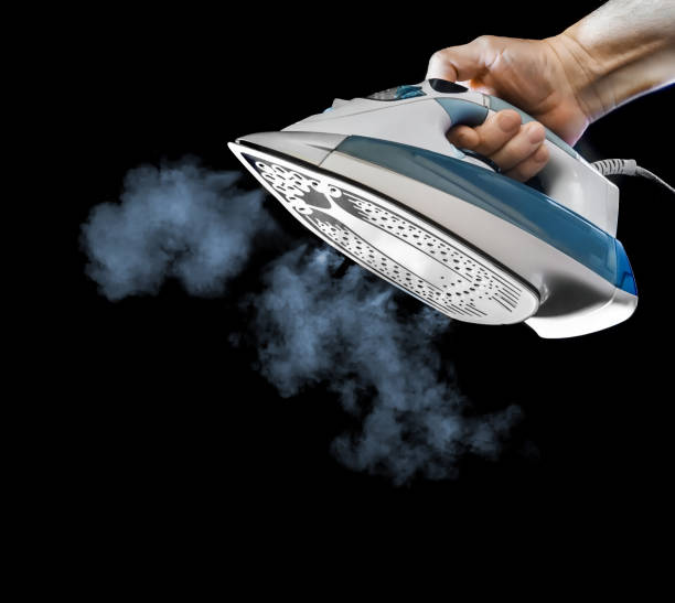 istock Hand holds an Iron with steam, isolated on black background 1481414299
