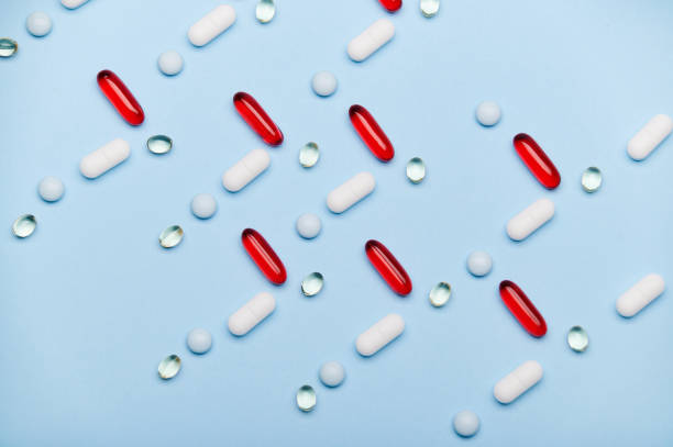istock Flat lay. Red gel translucent capsules, dragees, medical pills arranged in pattern on blue backdrop. Pharma business. 1481415555