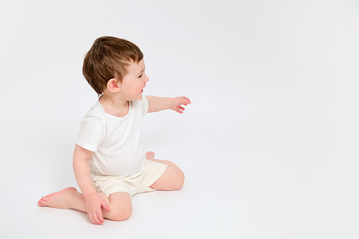 A happy baby is sitting on a studio white background. Full-length portrait of a smiling child. Kid aged about two years (one year nine months)