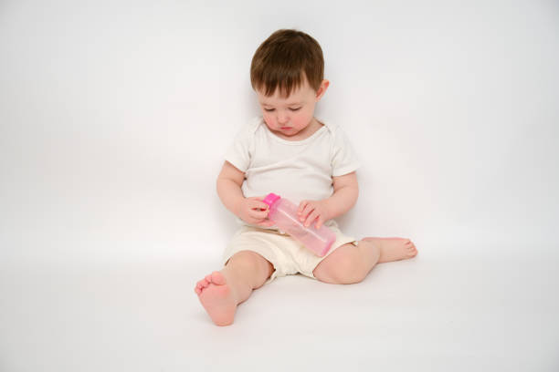 istock Baby breaks a milk bottle while pressing the nipple, studio white background. Kid about two years old (one year nine months) 1481415723