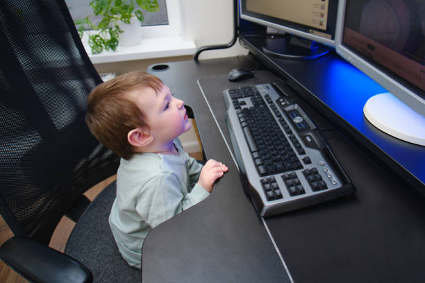 istock Happy baby is sitting at the computer keyboard next to the monitors. A child with a desktop PC in a home living room. Kid aged about two years (one year nine months) 1481415736