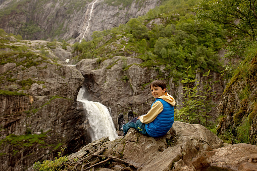 Happy european family with kids and dog, enjoying the hike to Manafossen waterfall summertime on a cold day