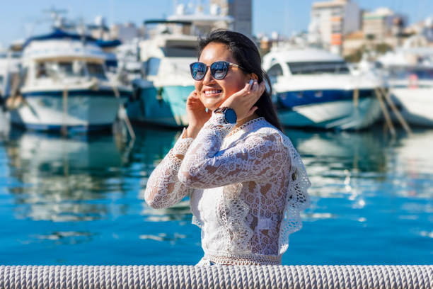 belle touriste asiatique souriant à la caméra avec des bateaux de luxe en arrière-plan - the mall audio photos et images de collection