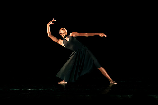 Black young woman performing contemporary dance on dark stage