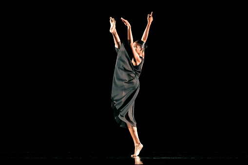 Black young woman performing contemporary dance on dark stage