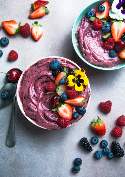 Two summer acai smoothie bowls with strawberries, blueberries,   on gray concrete background. Breakfast bowl with fruit and cereal, close-up, top view, healthy food