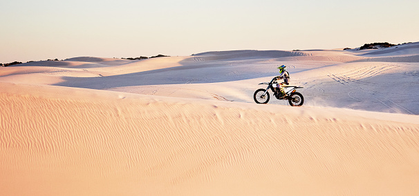 Desert, nature and athlete riding a motorcycle for exercise, fitness or skill training in nature. Extreme sports, action and male athlete on a bike for an outdoor workout in the sand dunes in Dubai.