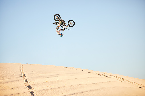 Motorcycle, jump and sports athlete in desert, dirt bike rally outdoor with extreme sport stunt, power and action. Nature, adventure and freedom, fitness challenge and biker person, mockup and travel