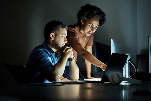 Two young business people working together on a laptop in their office late at night