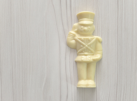 Closeup of mass produced white chocolate in the shape of a toy soldier against a whitewashed wood background with copy space.