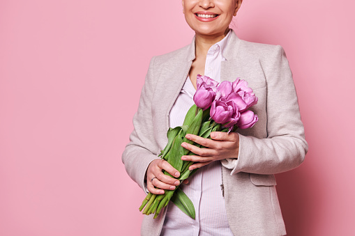 Details on a cute bouquet of purple tulips for festive occasion, in the hands of a beautiful smiling woman, isolated pink background, Happy Teachers, Mothers or International Women's . Spring concept