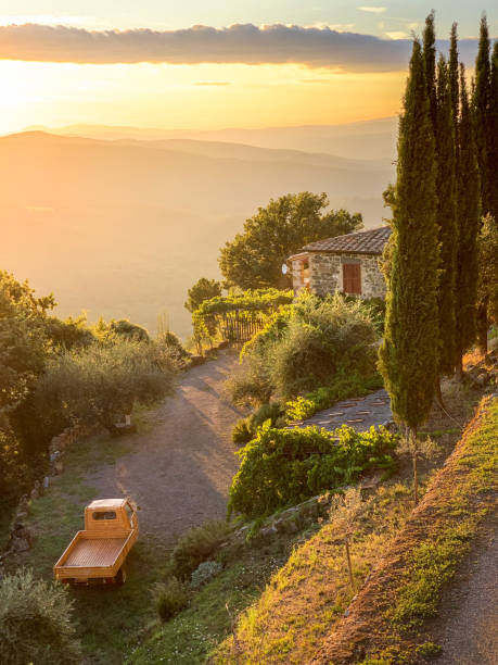 Sunset in Tuscany with old scooter truck Tuscan countryside stone house with orange three-wheeled pick-up scooter, tall cypress trees, and sunset light flooding distant rolling hills tuscany photos stock pictures, royalty-free photos & images
