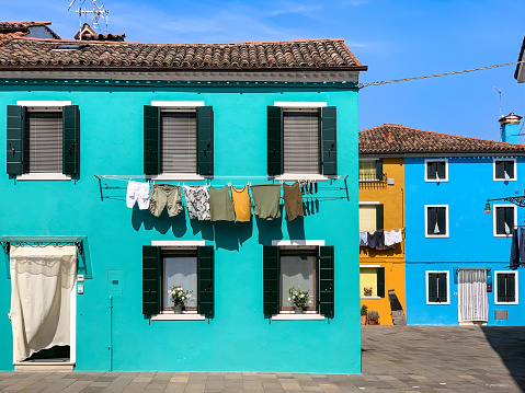 Teal, ochre, and blue houses on Burano island in Venetian lagoon famed for its houses painted in vivid colors on clear sky summer day