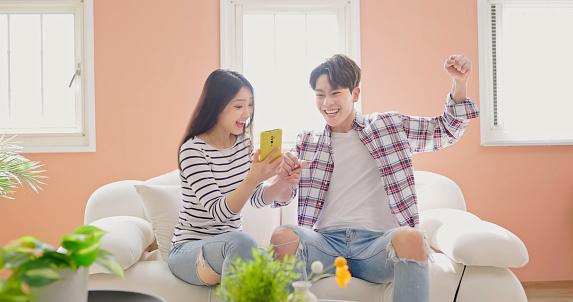 asian couple sitting on couch is looking mobile phone excitedly because they win the prize or make deal