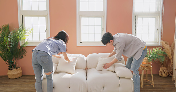 asian young couple are patting pillow on couch and it is fresh and comfortable