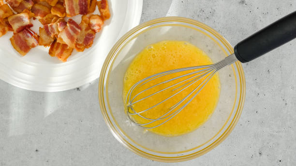 istock Whipped eggs in a glass bowl, and crispy fried bacon on a white plate close-up on a light grey background 1481444360