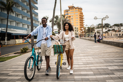 Young couple walking with bikes on the coastline