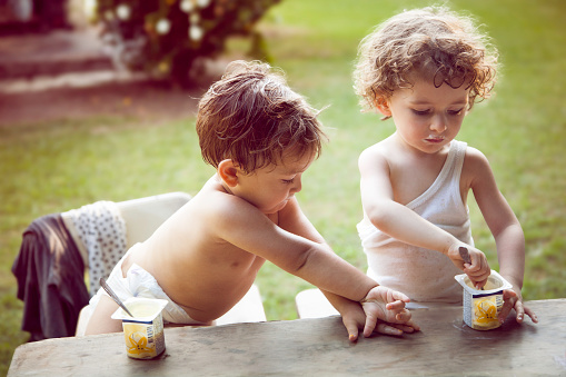 Two little children eating snack in a garden