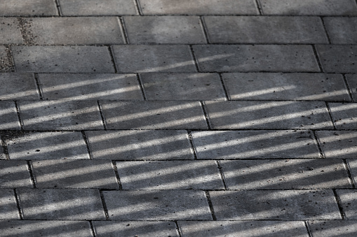 Gray concrete cobble road with striped shadows pattern, paving slabs background