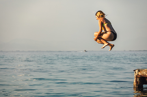 Teenage girl having fun on the sea. She jumps from a pier  into the blue sea