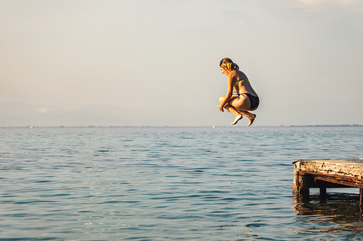 Teenage girl having fun on the sea. She jumps from a pier  into the blue sea