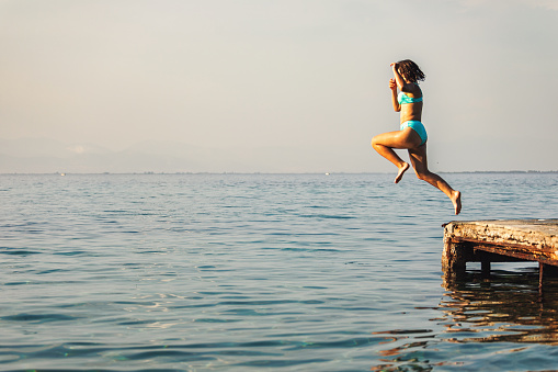 Teenage girl having fun on the sea. She jumps from a pier  into the blue sea