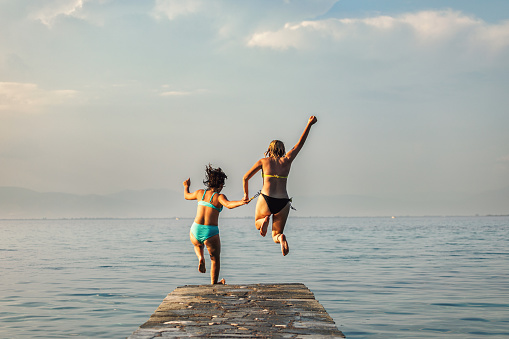 Sisters  having fun on the sea. They jumps from a pier  into the blue sea