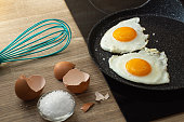 fried eggs in a frying pan, salt and eggshell on the table