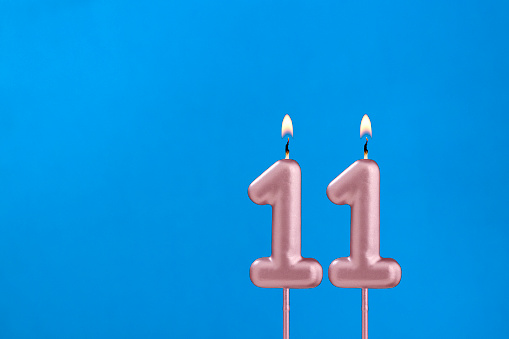 Number 11 - Burning anniversary candle on blue foamy background