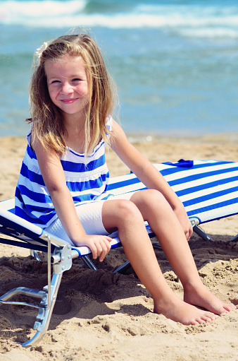A little girl is sitting on a sun lounger on the beach